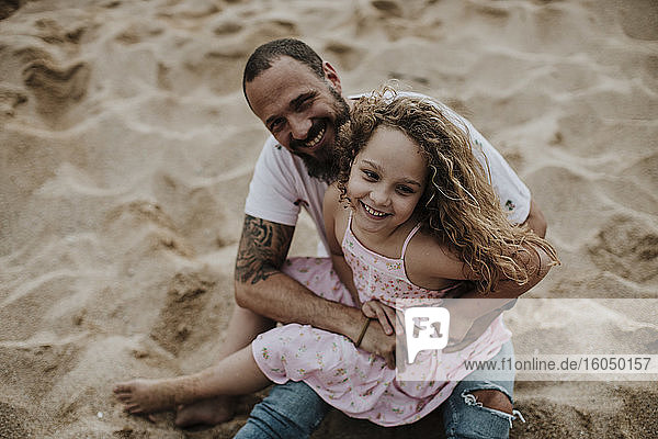 Tochter sitzt auf dem Schoß des Vaters und spielt am Strand