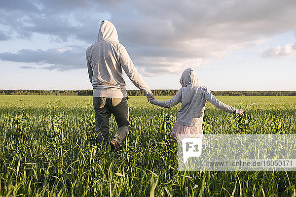 Father and daughter holding hands while walking amidst plants on landscape
