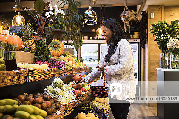 Junge Frau trägt Weidenkorb beim Kauf von Obst im Lebensmittelgeschäft