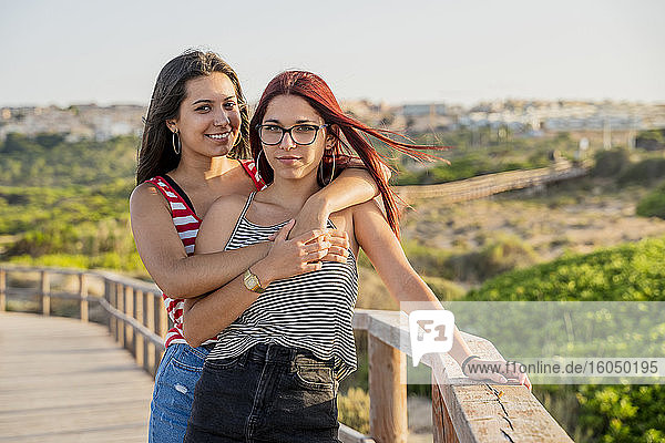 Zärtliche Teenager-Mädchen umarmen sich auf der Promenade am Strand gegen den klaren Himmel