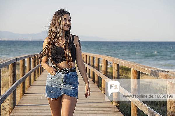 Schönes Teenager-Mädchen zu Fuß auf der Promenade am Strand gegen klaren Himmel