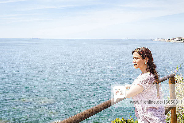 Woman leaning on railing while looking at Ligurian Sea against sky during sunny day