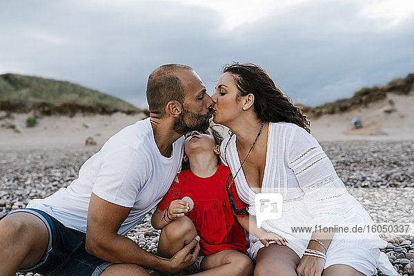 Couple kissing while sitting with daughter at beach