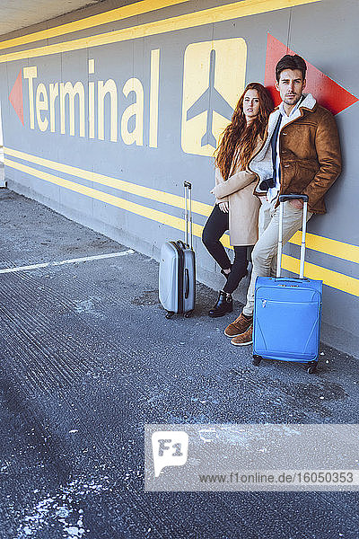 Confident business couple standing with luggage at airport terminal