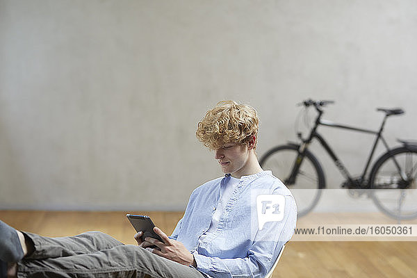 Junger Mann sitzend mit digitalem Tablet