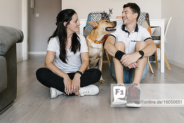Smiling couple enjoying with dog while sitting on floor at home