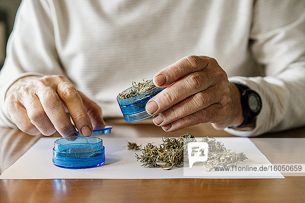 Midsection of senior man grinding weed in grinder at home