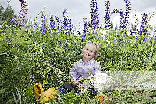Porträt eines glücklichen Mädchens  das vor einem Lupinenfeld mit einem Strauß gepflückter Blumen sitzt