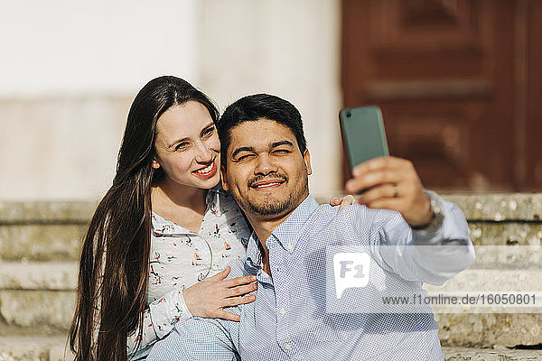 Glückliches schwangeres Paar  das ein Selfie mit seinem Smartphone an einem sonnigen Tag macht