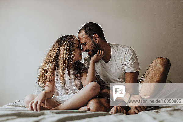 Vater und Tochter reiben sich zu Hause auf dem Bett die Nasen