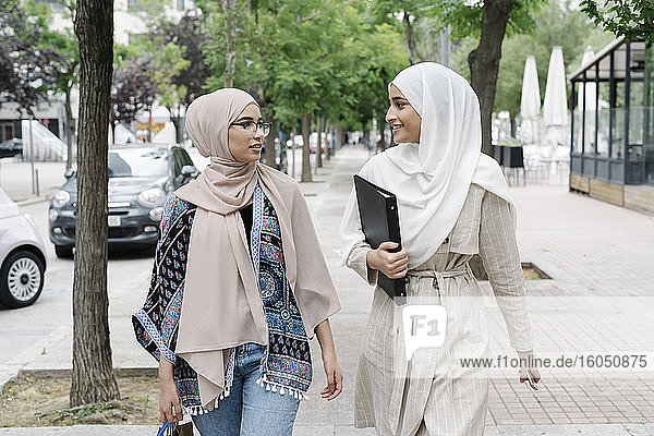 Muslim sisters talking while walking on sidewalk