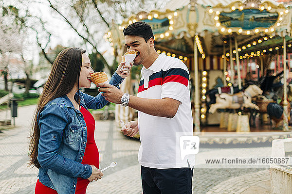 Happy expectant couple feeding ice creams to each other outside amusement park  Cascais  Portugal