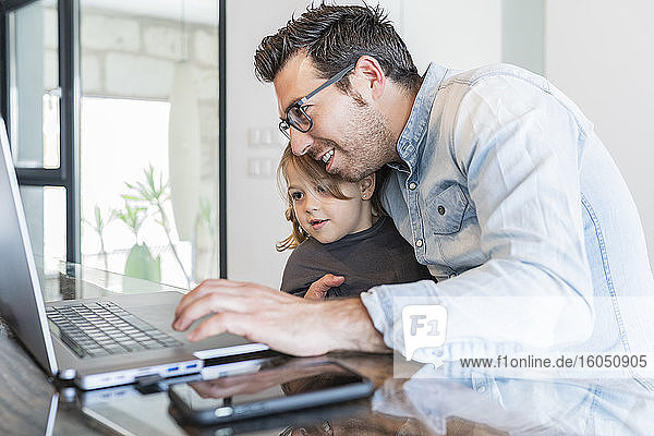 Vater umarmt Tochter bei der Arbeit am Laptop zu Hause