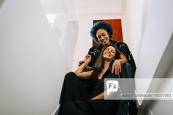 Happy female friends wearing black clothing sitting on steps at home