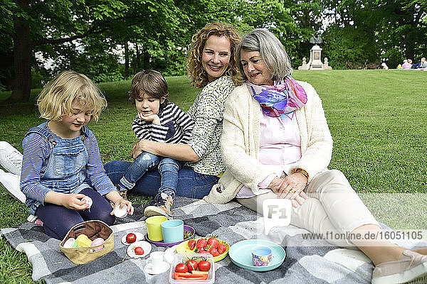 Glückliche Kinder genießen ihr Picknick mit Mutter und Großmutter im öffentlichen Park