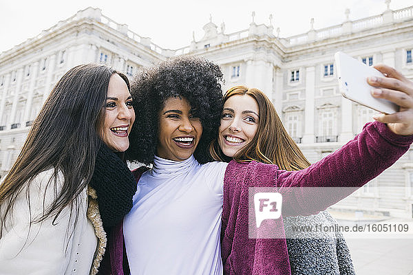Glückliche junge Frau  die ein Selfie mit ihren Freundinnen macht  während sie vor dem Königspalast in Madrid steht  Spanien