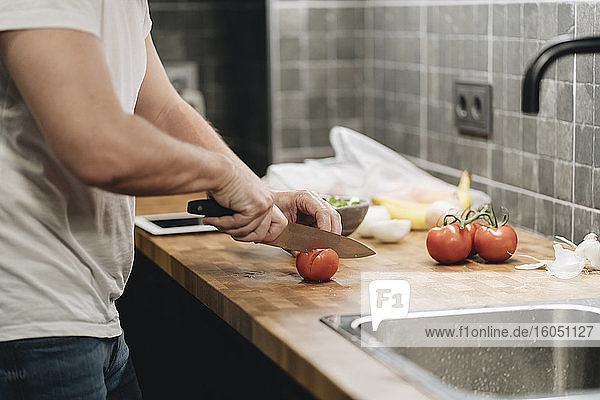 Älterer Mann steht in der Küche und schneidet Tomaten