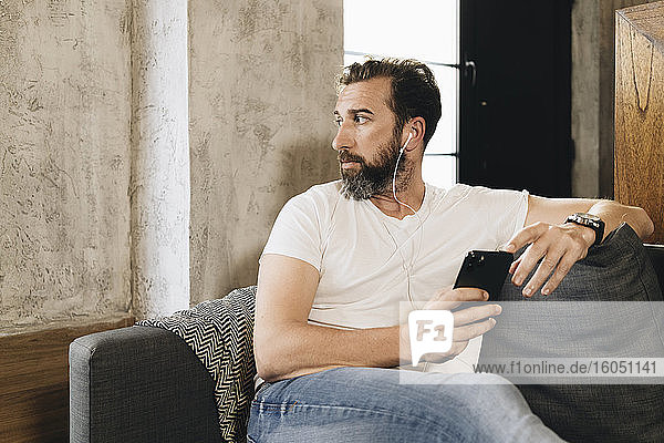 Mature man sitting on couch  using smartphone