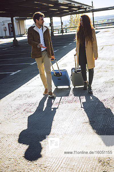 Business couple pulling luggage at airport parking lot during sunny day