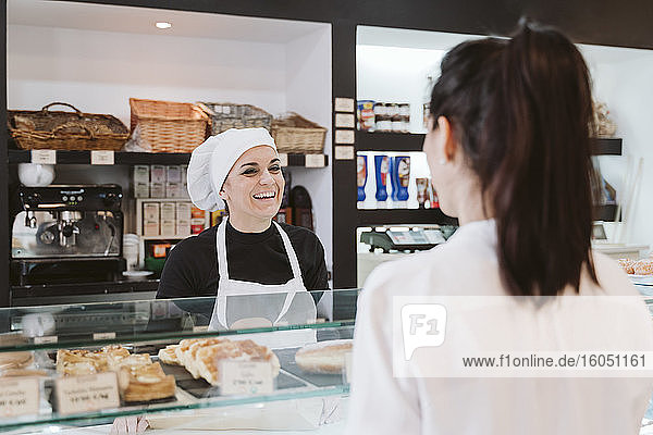 Happy female baker attending customer at bakery