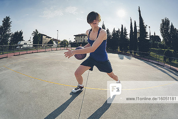 Teenager-Mädchen übt Basketball auf dem Platz gegen den Himmel