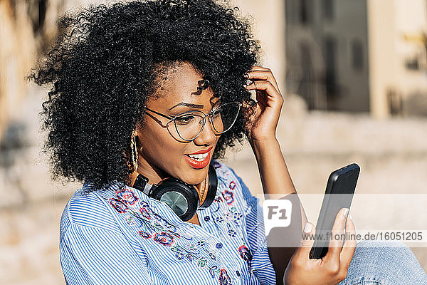 Lächelnde Frau mit Afro-Haar und Brille während eines Videoanrufs im Freien