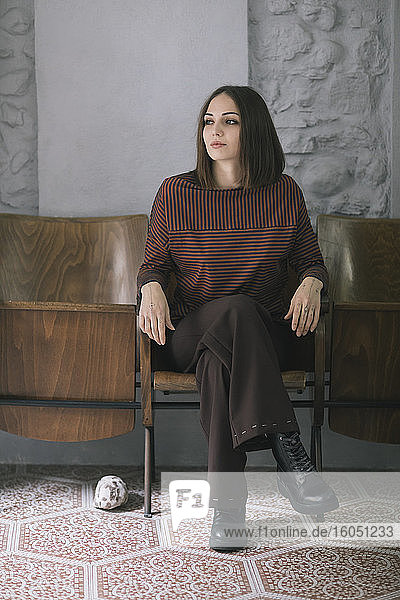 Nachdenkliche schöne Frau sitzt auf einem Stuhl im Atelier für Bekleidungsdesign