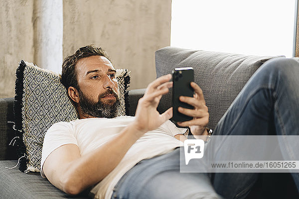 Mature man lying on couch  using smartphone