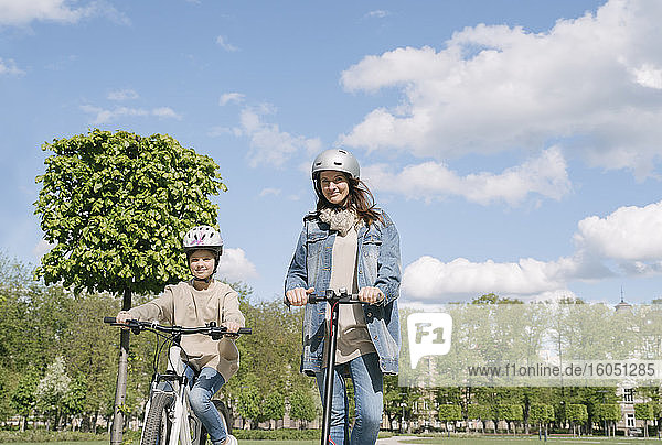 Mädchen auf dem Fahrrad  während die Mutter auf dem Motorrad gegen den Himmel im Stadtpark fährt
