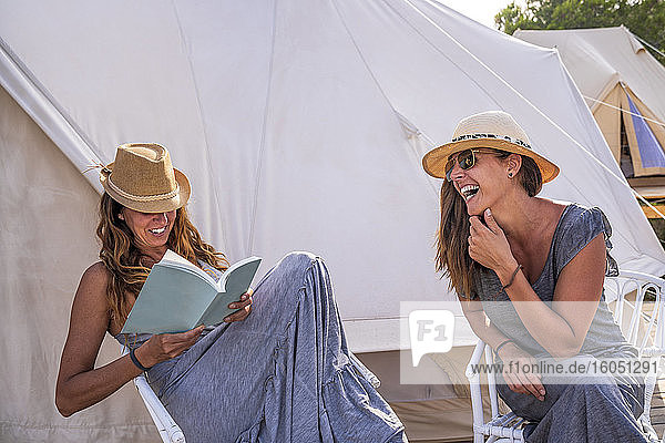 Fröhliche Frau  die lacht  während ihr Freund auf dem Campingplatz ein Buch liest