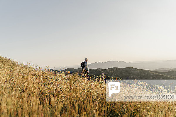 Aktiver älterer Mann  der die Landschaft betrachtet  während er auf einem Berg steht