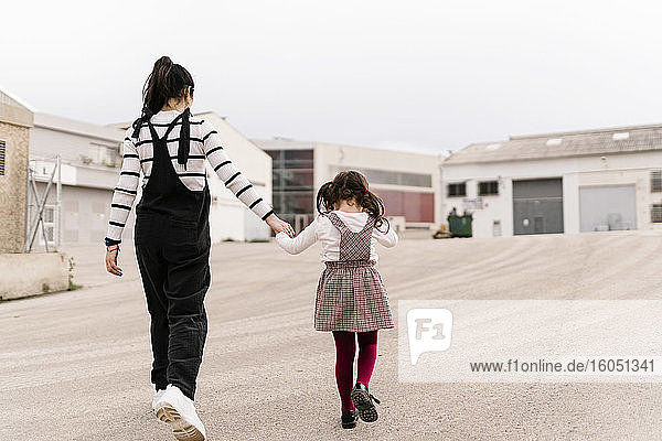 Mutter und Tochter halten sich beim Gehen auf der Straße an den Händen