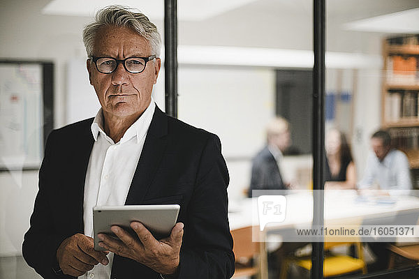 Senior businessman using digital tablet  coworkers working in background