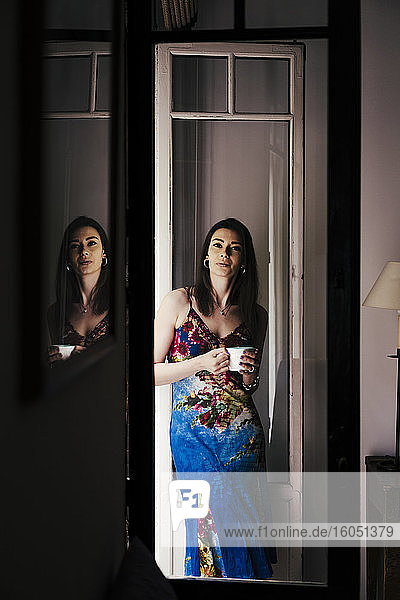 Frau mit Kaffeetasse  die sich zu Hause an die Tür lehnt