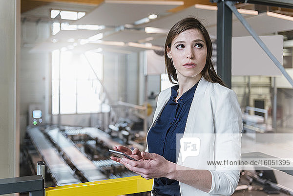 Weiblicher Manager  der ein digitales Tablet hält und wegschaut  während er in einer Fabrik steht