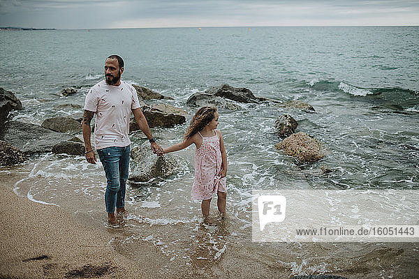 Vater und Tochter halten sich am Strand an den Händen