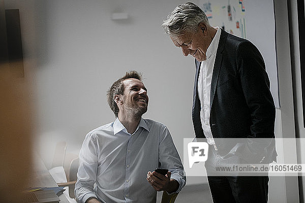 Senior businessman listening to younger business partner  holding smartphone