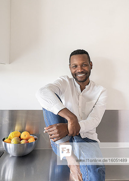Porträt eines lächelnden Mannes  der zu Hause auf dem Küchentisch sitzt