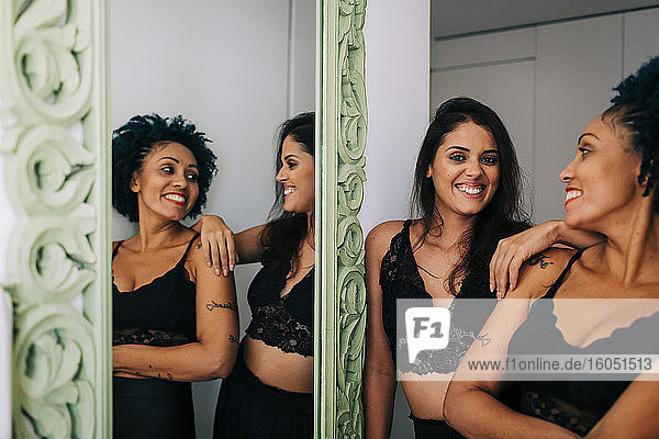 Happy female friends wearing black clothing standing by mirror at home