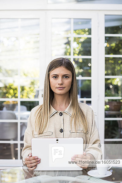 Selbstbewusste junge Frau mit digitalem Tablet am Tisch in einem Café