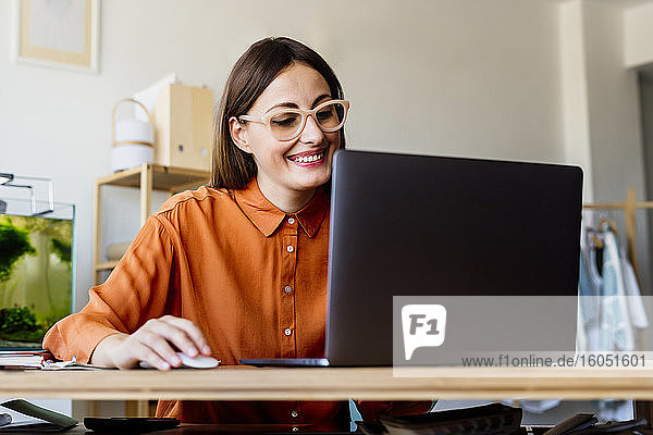 Weibliche Modedesignerin  die zu Hause am Schreibtisch sitzt und einen Laptop benutzt