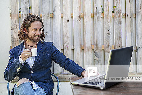 Gutaussehender junger Geschäftsmann trinkt Espresso und benutzt einen Laptop in einem Cafe