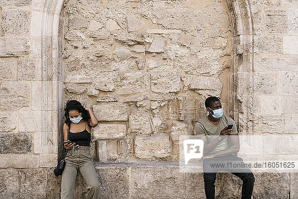 Mann und Frau tragen Masken und benutzen Smartphones an der Wand