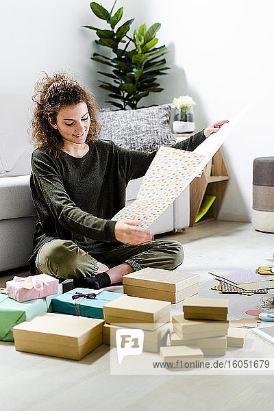 Lächelnde junge Frau  die zu Hause auf dem Boden sitzt und Geschenke einpackt