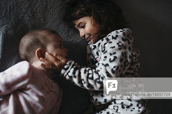 Mädchen berührt die Wangen ihrer kleinen Schwester  während sie auf dem Bett liegt