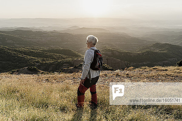 Aktiver älterer Mann steht auf einem Berg und betrachtet die Landschaft bei Sonnenuntergang