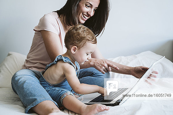 Mutter und kleines Mädchen benutzen Laptop auf dem Bett zu Hause