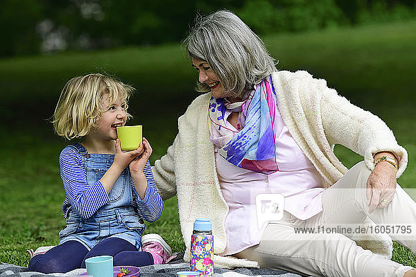 Glückliche Großmutter sieht ihre Enkelin an  die beim Picknick im Park Wasser trinkt