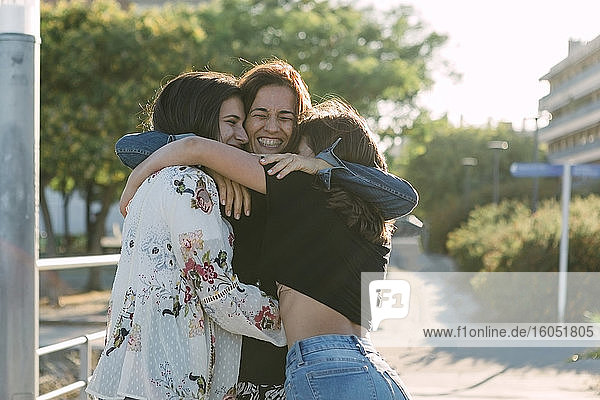 Cheerful mother embracing daughters while standing outdoors