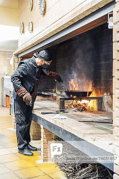 Traditionelle Zubereitung von Paella in einer Restaurantküche  der Koch trägt eine Schutzmaske
